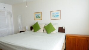 A bedroom with a bed, two green pillows, a wooden nightstand, a wooden cabinet, and two framed pictures on the wall. - Oceanfront retreat in with AC and pool (Inch Marlow)
