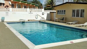 A rectangular swimming pool with a white edge, a ladder, and a lifebuoy. There are lounge chairs and a small table on the poolside. - Oceanfront retreat in with AC and pool (Inch Marlow)