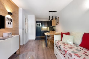 Un espacio habitable compacto con kitchenette, comedor y sofá con ropa de cama estampada.