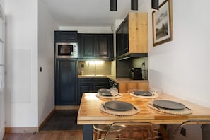 Una cocina compacta con armarios oscuros, una mesa de comedor de madera con platos y vasos, y un cuadro enmarcado en la pared.