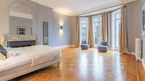 Ein großzügiges Schlafzimmer mit einem großen Bett, einem Kamin, Blick auf die Stadt durch große Fenster und einem modernen Design.