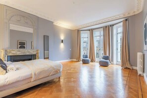 Ein großzügiges Schlafzimmer mit einem großen Bett, einem Kamin, Blick auf die Stadt durch große Fenster und einem modernen Design.