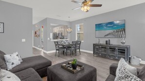 A modern living room with grey sofas, a dining area with a chandelier, and a kitchen in the background. - Headline (Davenport)