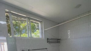 Ein Badezimmer mit weißem Waschbecken, einem Spiegel, einem Fenster und einer Duschkabine.