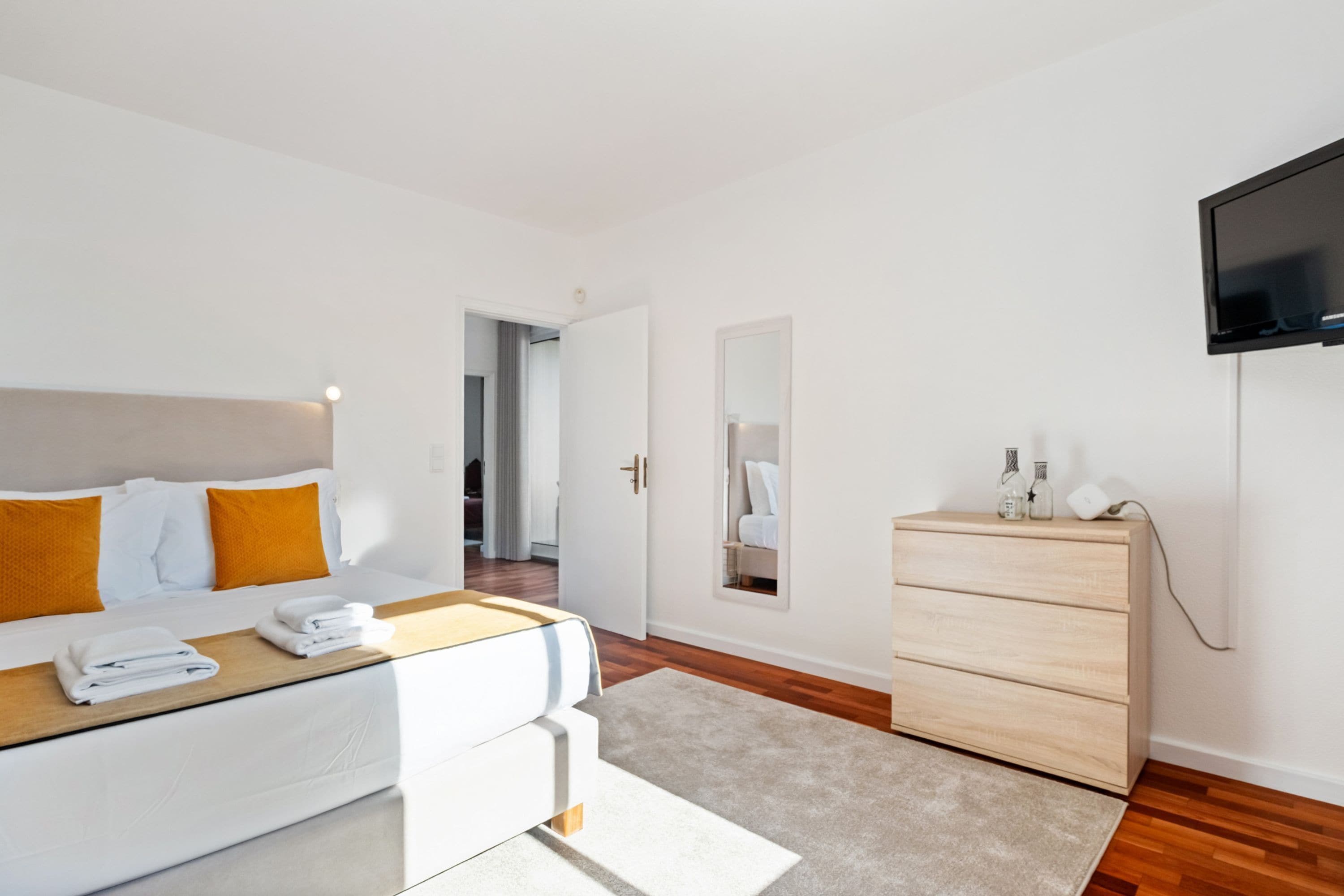 Una habitación de hotel moderna con cama, cómoda, televisor y espejo.