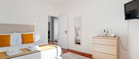Una habitación de hotel moderna con cama, cómoda, televisor y espejo.