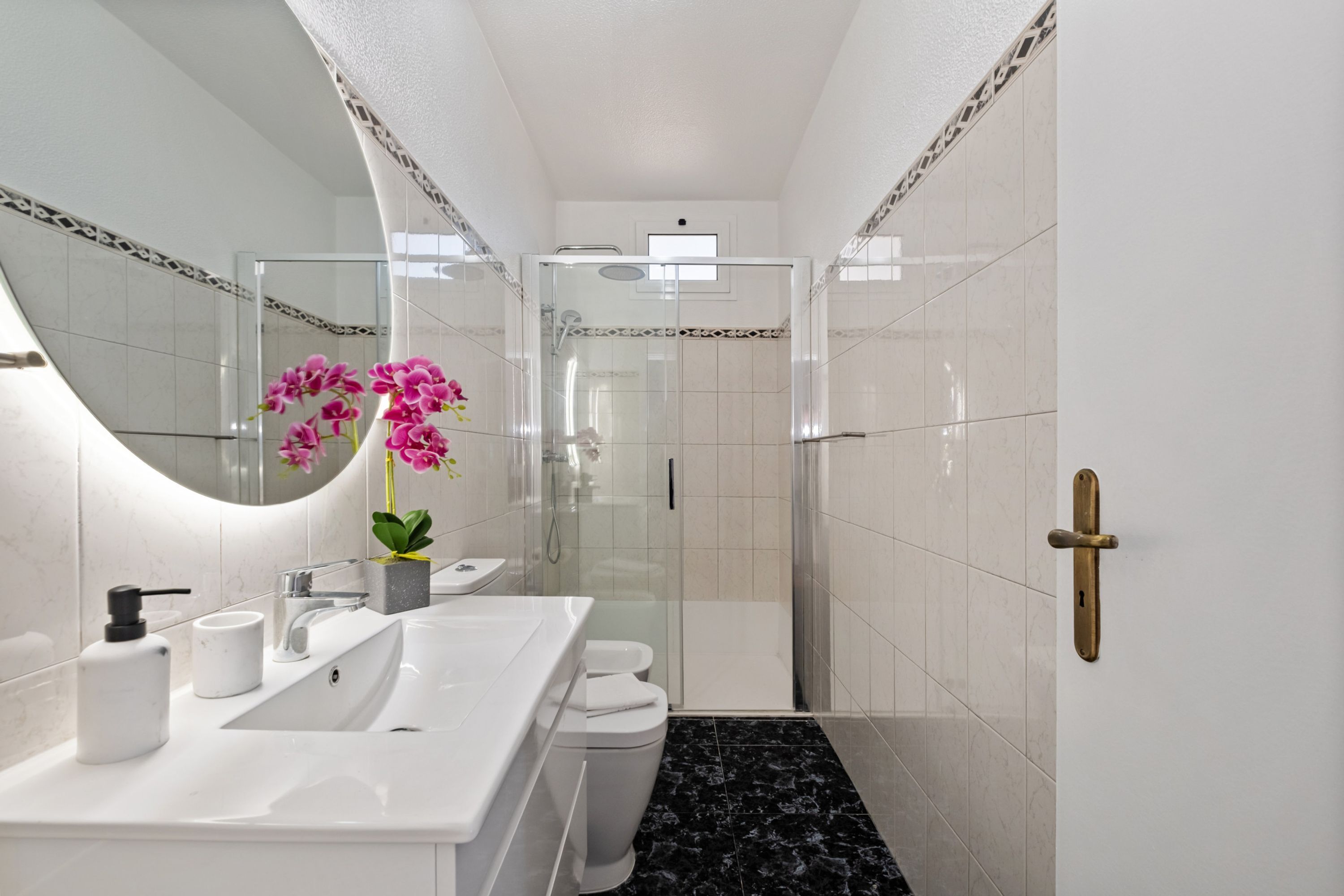 Ein modernes Badezimmer mit einer einteiligen Duschkabine, einem weißen Waschbecken mit Marmorplatte und einer Toilette.