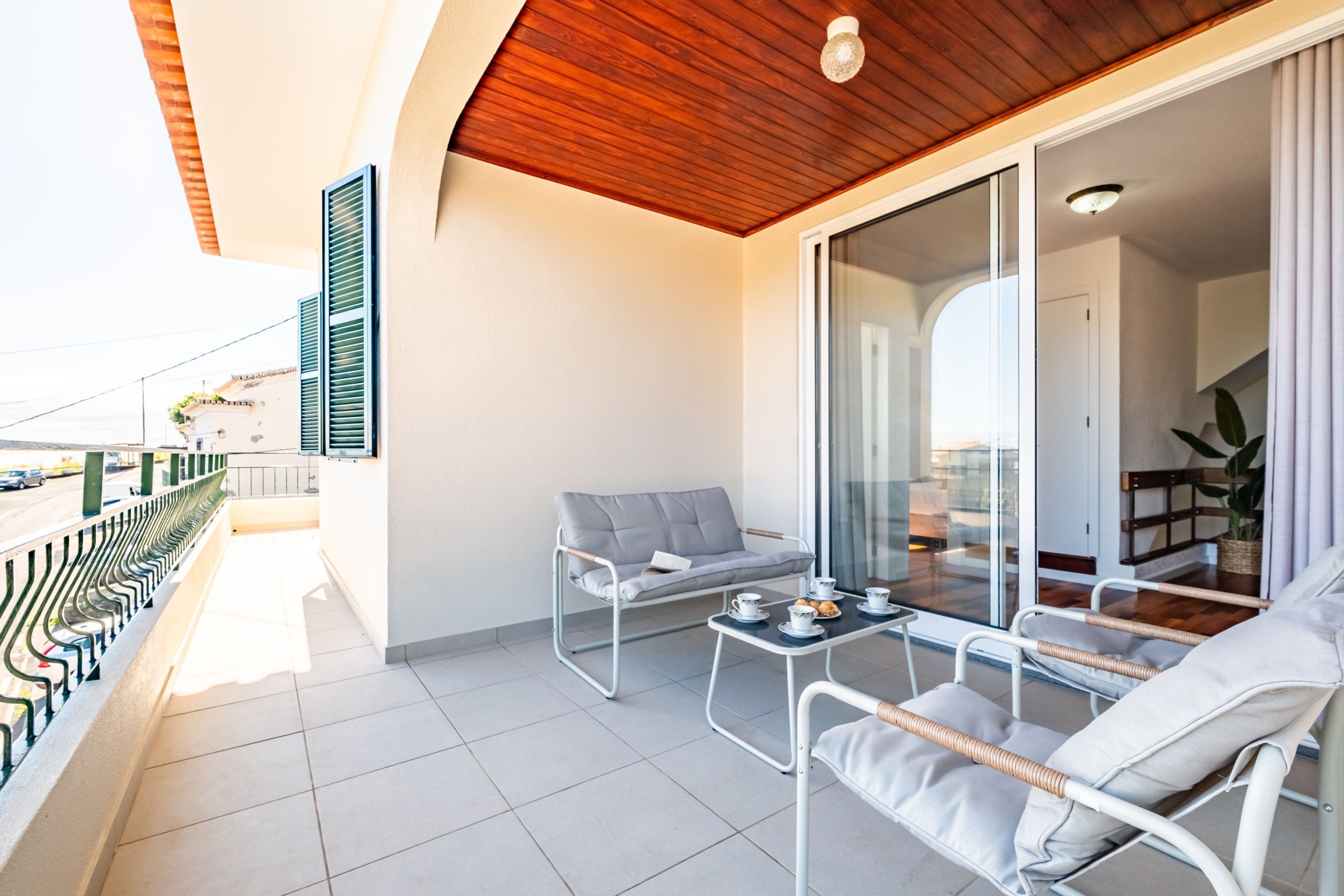 Un balcon avec un canapé, une petite table avec des tasses et des pâtisseries, et une vue sur la rue.