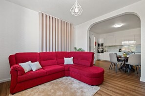 Uma sala de estar moderna com um sofá seccional vermelho, uma mesa de jantar de madeira e uma cozinha ao fundo.