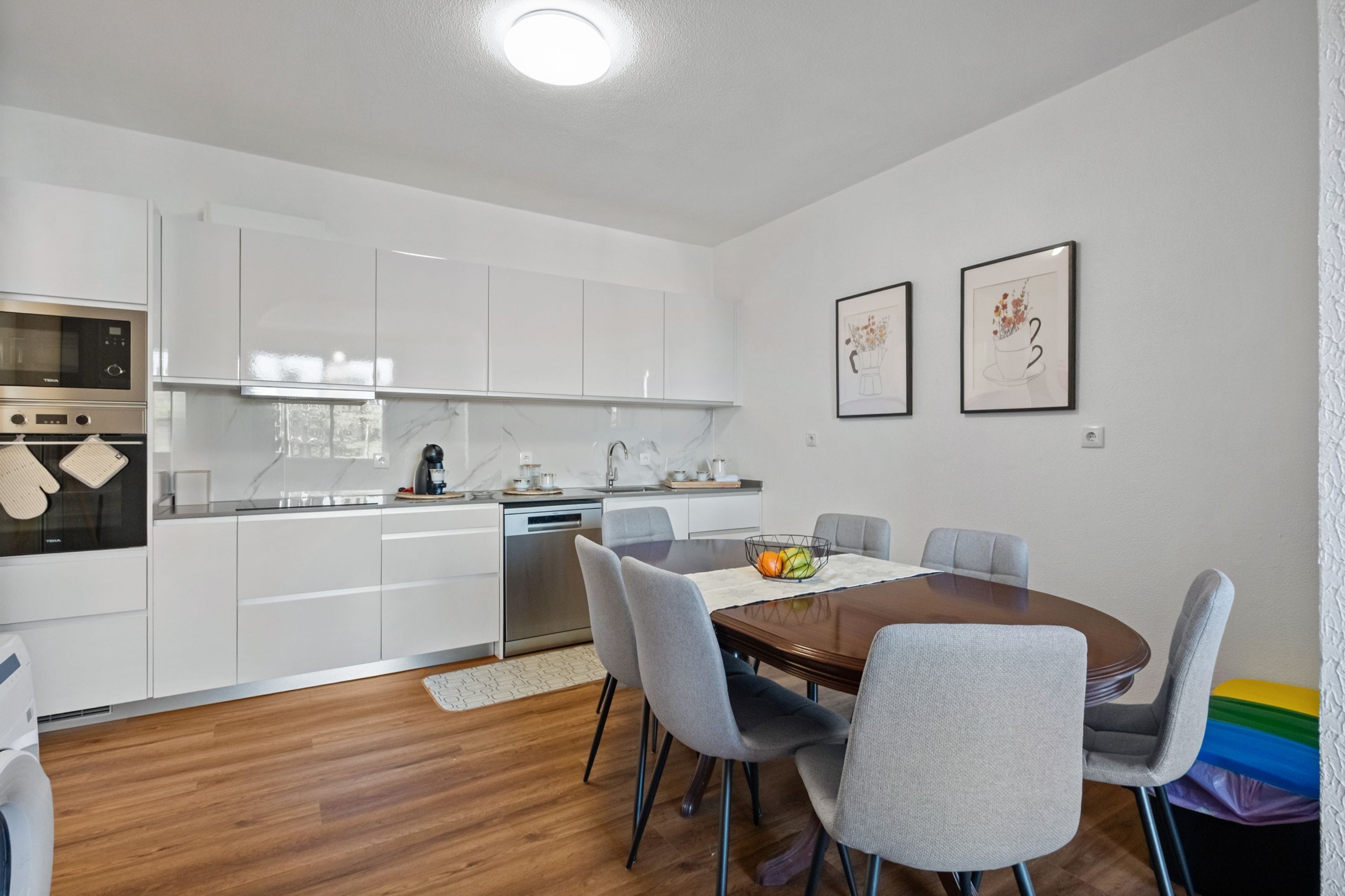Una cucina moderna con mobili bianchi, un tavolo da pranzo in legno e sedie grigie.
