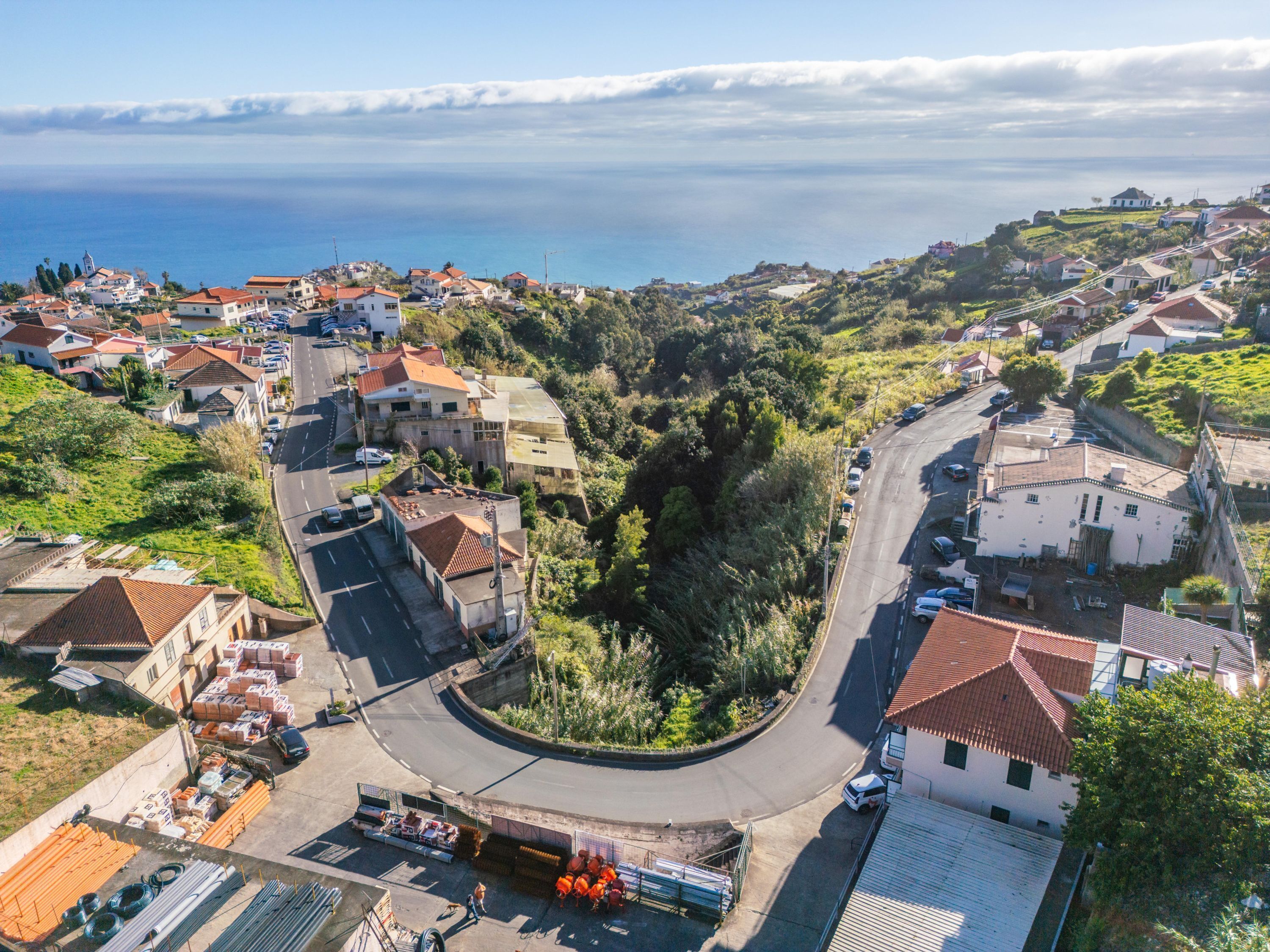 An aerial view of a coastal town with houses, a winding road, and a clear view of the sea.
