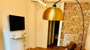 A modern living room with a round white table, white chairs, a brown leather sofa, a flat-screen TV on a white stand, and a patterned wallpaper. - BIG Design Portello Milano (Milano)