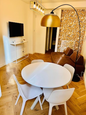 A modern living room with a round white table, white chairs, a brown leather sofa, a flat-screen TV on a white stand, and a patterned wallpaper. - BIG Design Portello Milano (Milano)