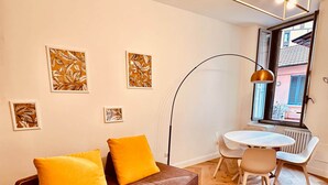 A modern living room with a brown sofa, two yellow cushions, a round dining table with two chairs, and a large window with a view of buildings. - BIG Design Portello Milano (Milano)