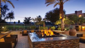 Un patio al aire libre con una chimenea de piedra, mobiliario de mimbre y palmeras.