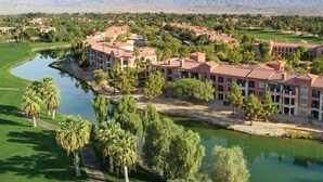 Un campo de golf con un complejo de edificios grande al frente, rodeado de árboles y una masa de agua.