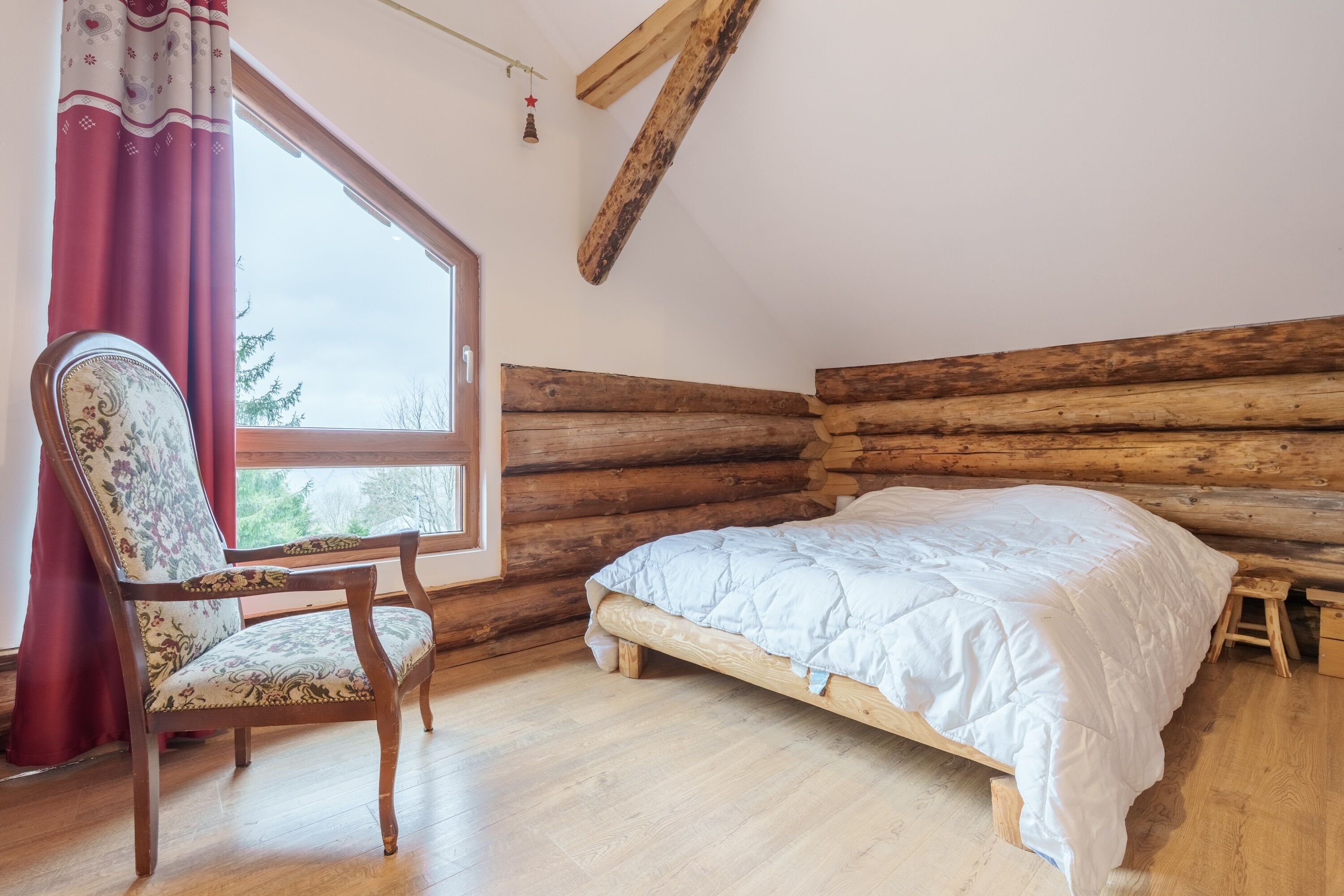 A log cabin bedroom with a wooden bed, a chair, and a window with curtains.