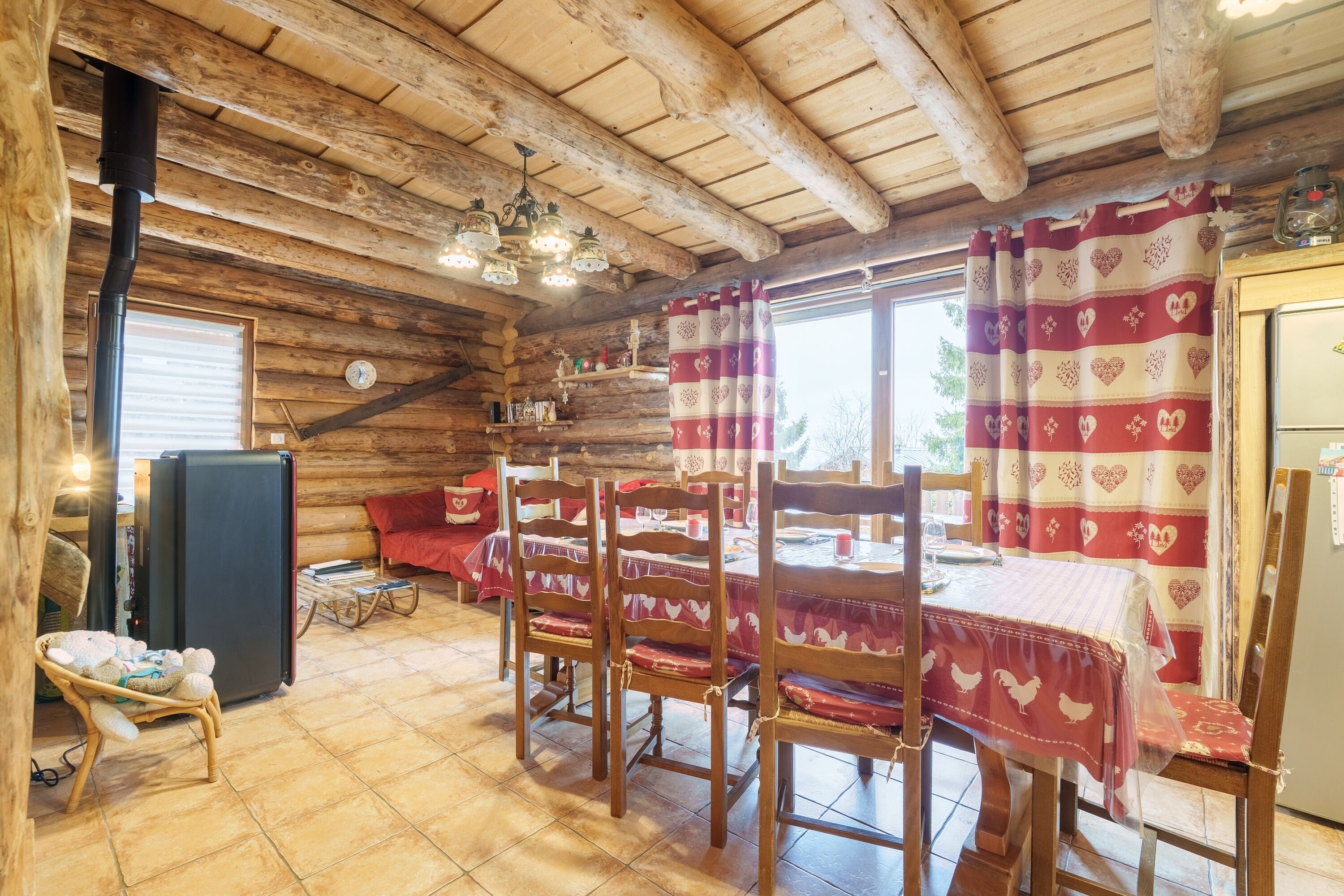 A rustic wooden interior with a dining table, chairs, and a refrigerator.