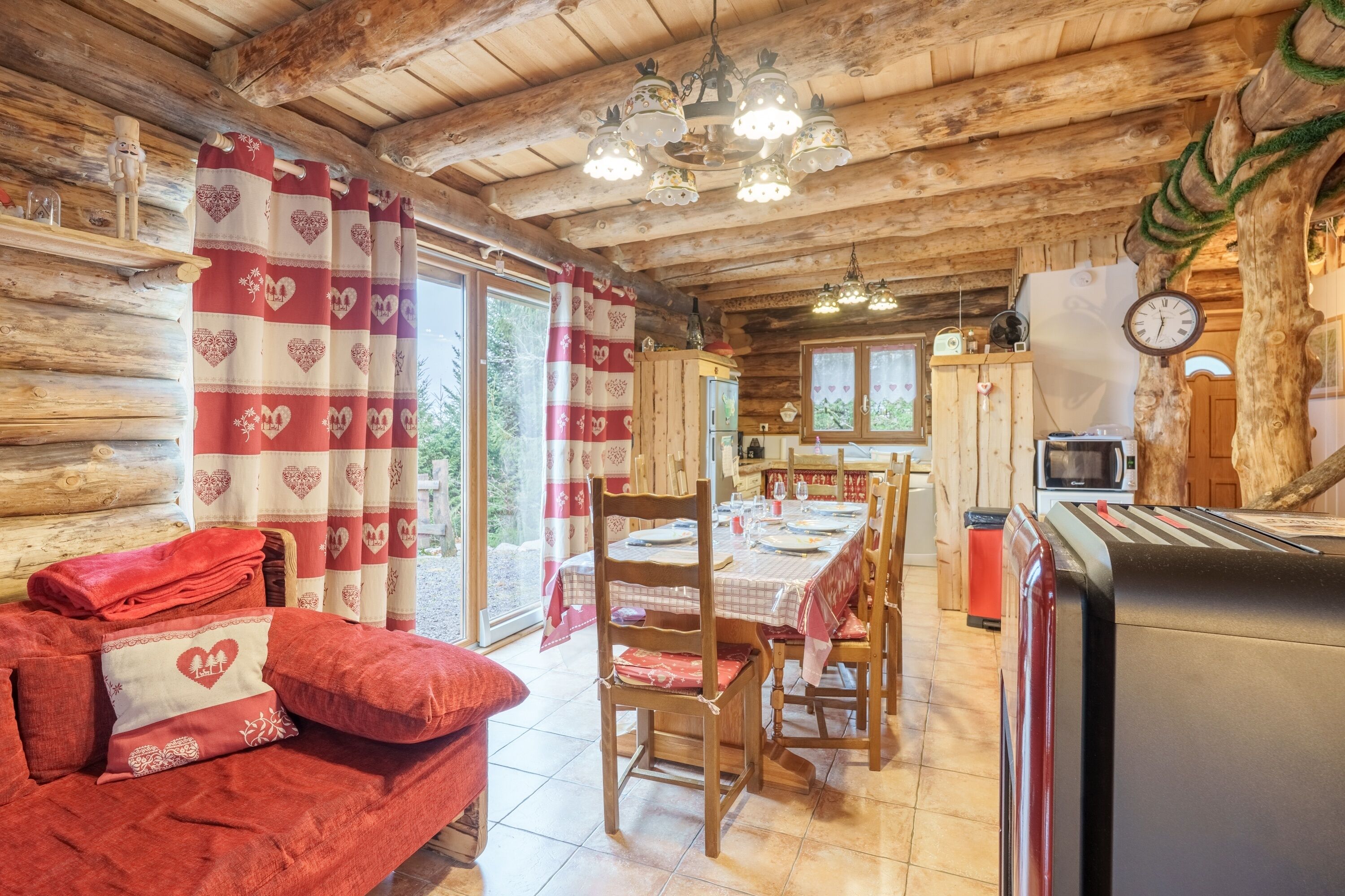 L’intérieur d’un chalet confortable, avec une salle à manger, une cuisine et un canapé rouge agrémenté de coussins à motifs de cœur.