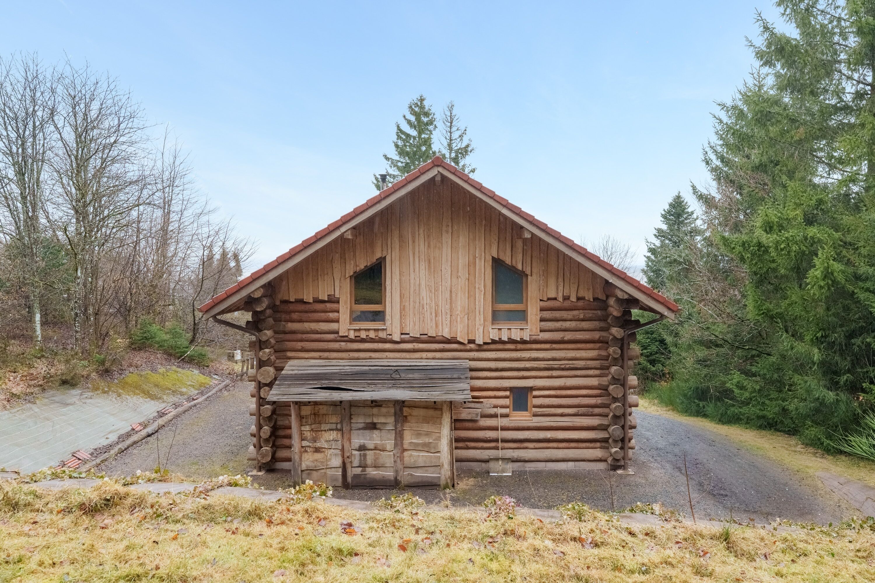 Une cabane en rondins avec un toit à pignon, deux fenêtres et une porte d’entrée.