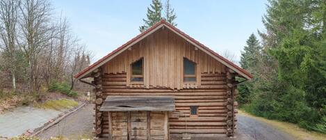 Une cabane en rondins avec un toit à pignon, deux fenêtres et une porte d’entrée.