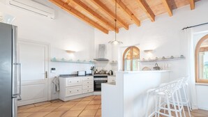 Una cocina con armarios blancos, techo de madera y piso de baldosas.