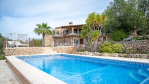 Una piscina con paredes de piedra, una escalera de piedra y un edificio con tejado de tejas y ventanas.