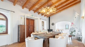 Un espacio amplio con una gran mesa de comedor de madera, sillas blancas, techo de madera y vistas al exterior.