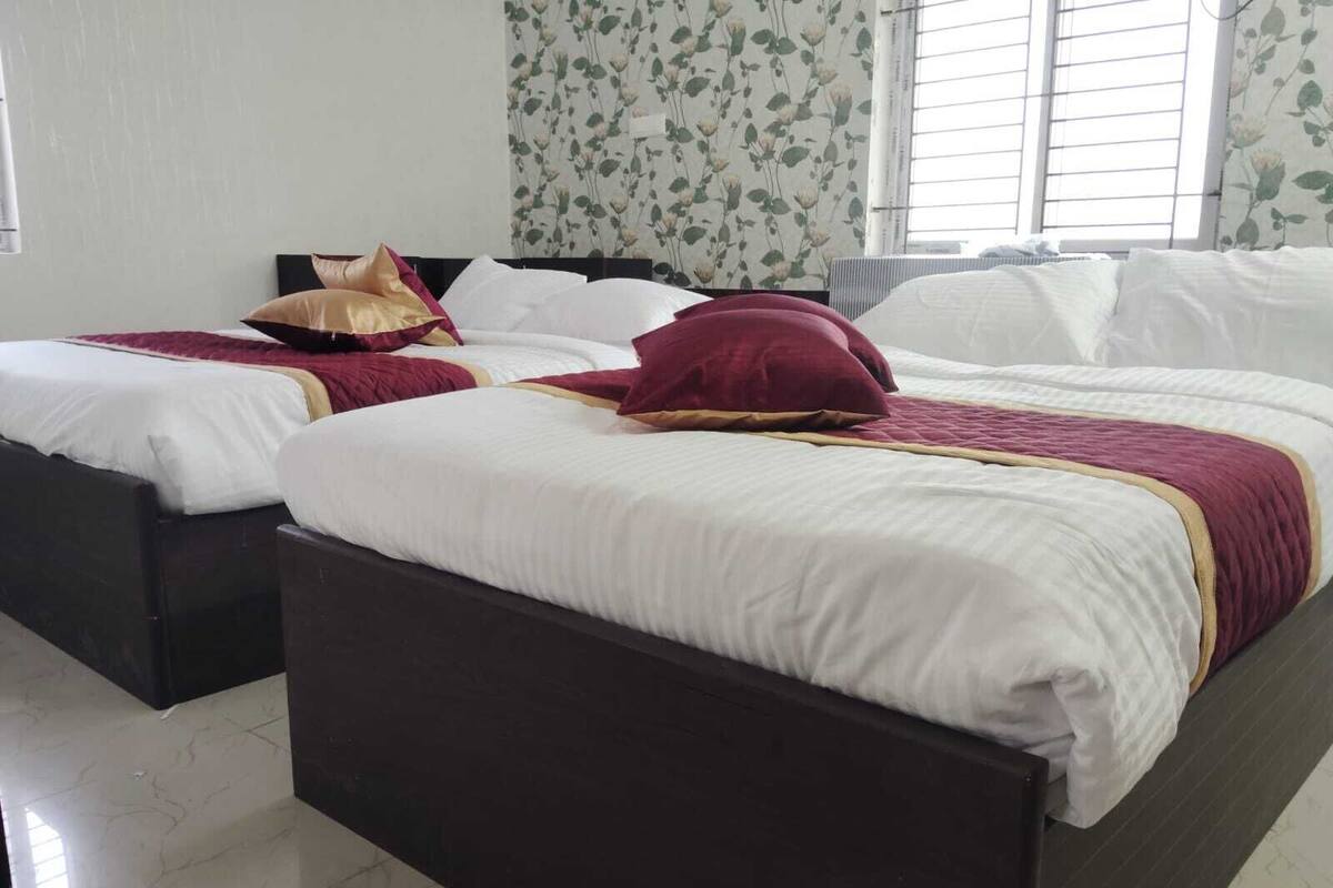 Une chambre d’hôtel avec deux lits, une grande fenêtre avec des stores et un papier peint à motifs floraux.
