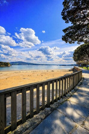 Ein Strand mit Holzzaun, blauem Himmel und sanften Hügeln in der Ferne.