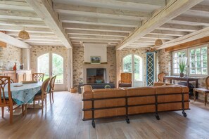 Un intérieur rustique avec des poutres apparentes, un canapé, une table à manger avec des chaises et de grandes fenêtres.