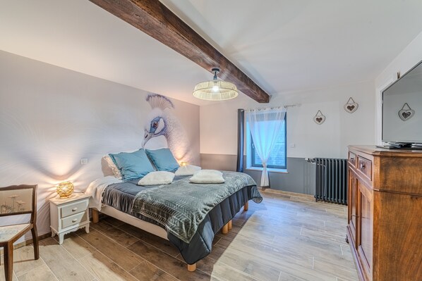 A bedroom with a bed, bedside table, lamp, and a large window with curtains.