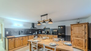A modern kitchen with wooden cabinets, a central island, and a dining area with white chairs.