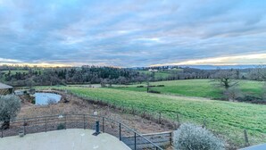 A rural landscape with a pond, fenced area, and distant hills.