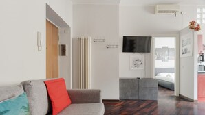 A modern living room with a grey sofa, a red pillow, a television, and a radiator. - GuestHost - Cozy 50m2 apartment located on the second floor of a building with lift, ideal for 4 people.The area is well equipped with the main services and allows you to quickly reach the most important attractions thanks to the presence of various bus, (Milan)