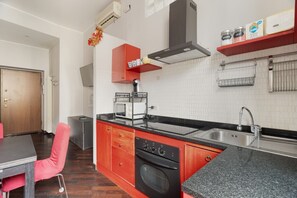 Une cuisine avec un plan de travail noir, des placards rouges, un four à micro-ondes et une cuisinière.