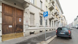 A street with a parked car, a building with a large wooden door, and a parking sign. - GuestHost - Cozy 50m2 apartment located on the second floor of a building with lift, ideal for 4 people.The area is well equipped with the main services and allows you to quickly reach the most important attractions thanks to the presence of various bus, (Milan)