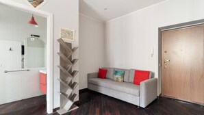 A room with a grey sofa, a wooden door, a white wall, and a staircase. - GuestHost - Cozy 50m2 apartment located on the second floor of a building with lift, ideal for 4 people.The area is well equipped with the main services and allows you to quickly reach the most important attractions thanks to the presence of various bus, (Milan)
