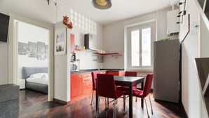 A modern kitchen with a dining area, wooden flooring, and a view through an open door. - GuestHost - Cozy 50m2 apartment located on the second floor of a building with lift, ideal for 4 people.The area is well equipped with the main services and allows you to quickly reach the most important attractions thanks to the presence of various bus, (Milan)