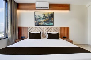 Une chambre d’hôtel avec un grand lit, un climatiseur fixé au mur, un tableau accroché au mur et une table de chevet avec un téléphone et une lampe.