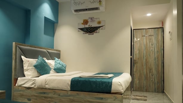 A bedroom with a bed, a wooden headboard, a wall-mounted air conditioner, and a door with a wooden panel. - Hotel New 7AM  (Mumbai)