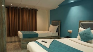 A hotel room with two beds, a wooden headboard, a blue accent wall, and a curtain. - Hotel New 7AM  (Mumbai)
