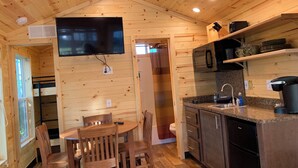 Een houten chalet van binnen, met een eethoek, keuken en een aan de muur bevestigde televisie.