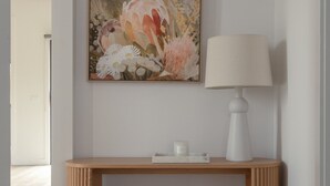 Ett stilrent, minimalistiskt konsolbord med en vit lampa och en blomstermålning ovanför.