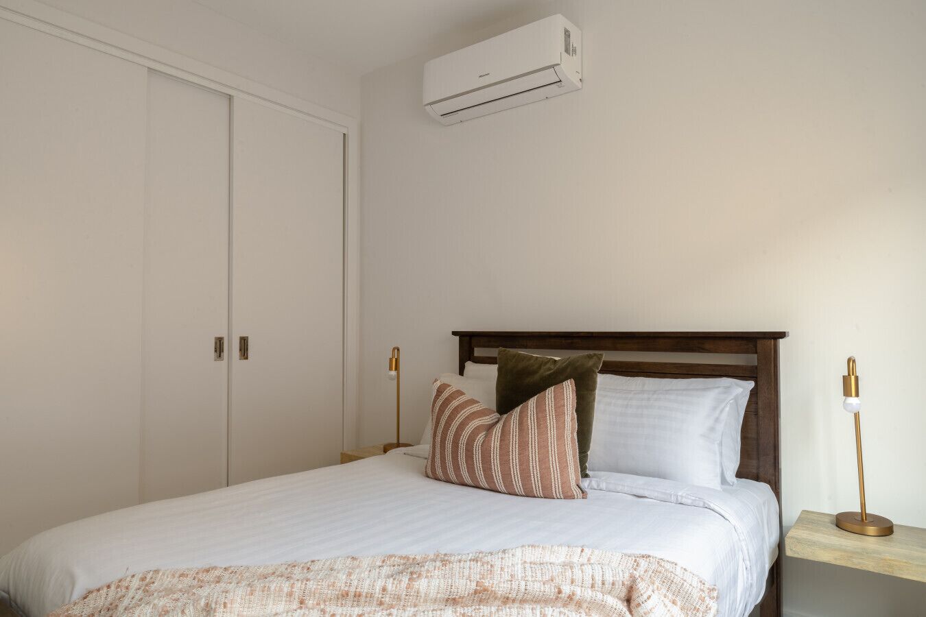 A bedroom with a bed, a nightstand, a lamp, and an air conditioning unit.