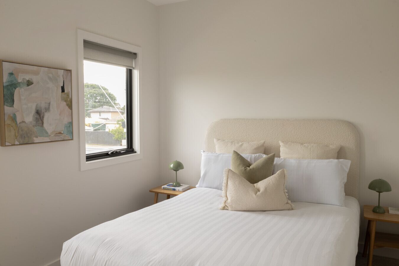 Une chambre avec un grand lit, une fenêtre donnant sur un beau paysage, une table de chevet avec une lampe et une œuvre d’art abstraite accrochée au mur.