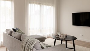 Ett modernt vardagsrum med en grå soffa, ett runt soffbord och en platt-TV som är monterad på väggen.