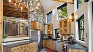 A modern kitchen with stone walls, wooden cabinets, and a stainless steel refrigerator. - Adullam Nature Escape - 10 acres in Colbert WA (Colbert)