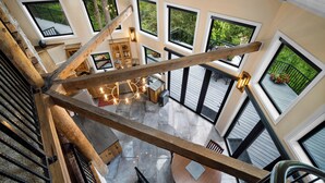 A spacious interior with a high ceiling, large windows offering views of greenery, and a central wooden beam structure. - Adullam Nature Escape - 10 acres in Colbert WA (Colbert)