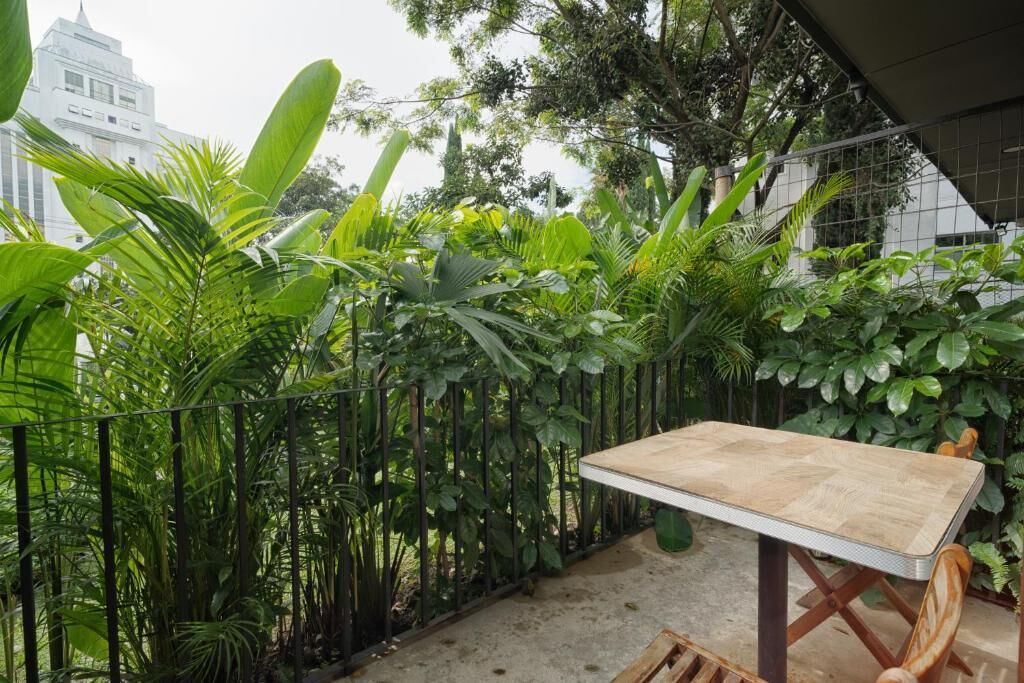 Una mesa y sillas dispuestas al aire libre, con una valla metálica y abundante vegetación de fondo.